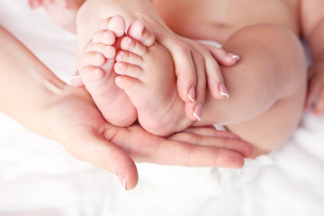 Fototapeta na wymiar Newborn baby feet in mother hands on white bed