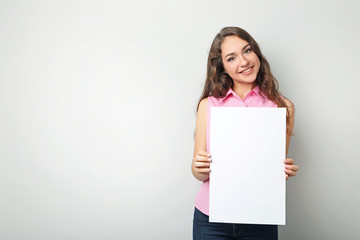 Fototapeta na wymiar Young woman with blank paper on grey background