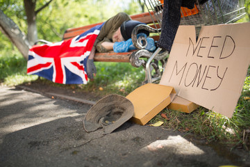 Homeless old man sleeping on bench, begging for money. Belongings of homeless male on ground close...