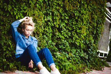 young beautiful woman in jeans clothes outdoors. portrait of a girl with freckles on her face, stylish girl against background of green leaves of a climbing plant, on a sunny summer autumn day.