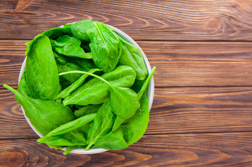 Fresh spinach leaves with water drops in ceramic bowl on the dark rustic wooden background....