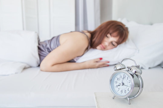A beautiful girl is sleeping in a white bed, a bright bedroom. Hours for eight hours. Good morning. Attractive woman
