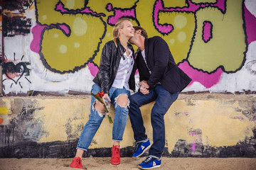 Couple in love embracing. Man kissing the woman in a neck, smilling girl sitting over the graffity background