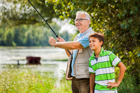 Grandfather and grandson are fishing on sunny day.