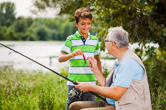 Grandfather and grandson are fishing on sunny day.