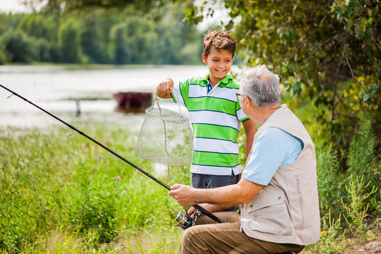 Grandfather and grandson are fishing on sunny day.