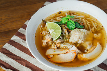 Noodle pork soup with Tom Yam spicy in white bowl on wooden table background.