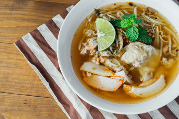 Noodle pork soup with Tom Yam spicy in white bowl on wooden table background.