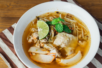 Noodle pork soup with Tom Yam spicy in white bowl on wooden table background.