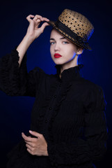 A beautiful, young, pale woman holds her hat. Gothic image, black blouse, mourning. Cold look, arrogance. A vampire.