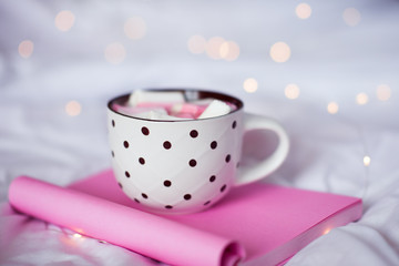 Morning cup of coffee with sweet marshmallow staying on open pink book close up. Selective focus.