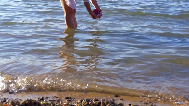 mother washing babies swimwear in sea water at beach. when done she walks out of water in slow-motion hd