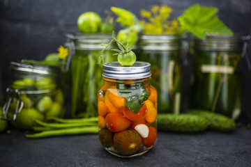 Jar of canned tomatoes and cucumbers jars on dark stone background.