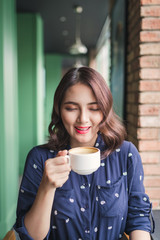 Portrait of happy young business woman with mug in hands drinking coffee in the morning at restaurant