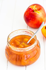 Nectarine (Peach, Apricot) jam confiture in glass jar and spoon on white wooden background. Vertical. Selective focus. Copy space for your text.