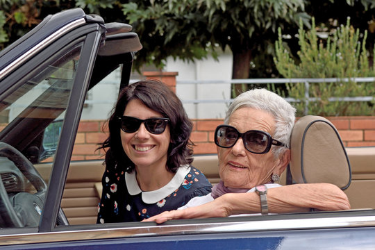 An Older Woman And A Young Woman Driving A Convertible