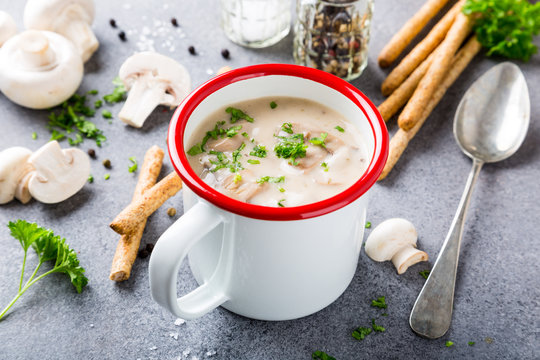 White enamel mug with delicious homemade mushrooms champignons soup with parsley. Healthy food concept.