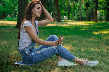 charming pretty girl sitting on the grass in the Park and listens to music