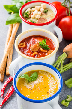 Assorted delicious homemade soups in enamel mugs with ingredients. Healthy food concept.