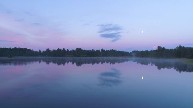 Aerial drone shot flying low over a misty and calm lake before dawn
