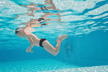Happy small boy swim underwater, has fun and dive in the blue transparent water of clear pool. Swimming classes and water safety education. Family vacation, weekend with kids © biotin