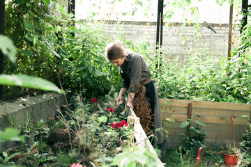 Young cute lady working at the greenhouse with wildflowers wearing linen dress and leather belt with florist tools