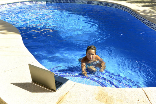 El ni&ntilde;o esta disfrutando el agua de la piscina mientras mirando su ordenador