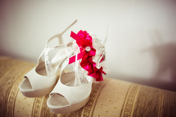 Bride's white shoes with garter stand on the sofa