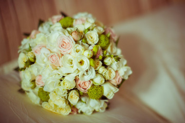 Green and white wedding bouquet of tiny roses lies on a bed