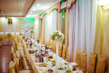 Long dinner table decorated with tall vases stands in the hall