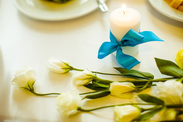 Obraz na płótnie Canvas Tender white roses lie before a candle with blue ribbon