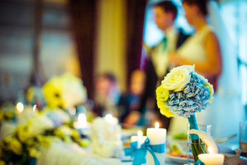 Bouquet of roses and blue hydrangeas stands on dinner table