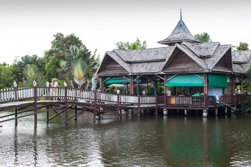 Fototapeta na wymiar Thai picturesque tropical landscape with wooden buildings and lake with a bridge and palms