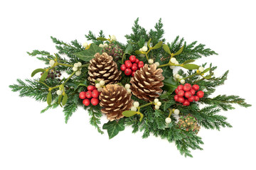 Christmas floral decoration with holly, gold pine cones, mistletoe, cedar cypress and juniper leaf sprigs and ivy on white background.
