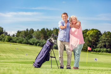 Senior couple giving thumbs up on a golf course.