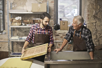Elderly artisan and young apprentice at work - obrazy, fototapety, plakaty