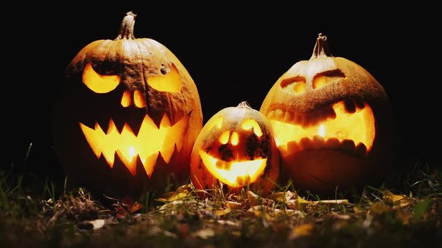 Three pumpkins on the grass at night with carved on them terrible faces. Light randomly illuminates them. Scary scene. Halloween pumpkin heads jack lantern