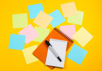 Colored note papers with a pen and notepads with a blank pages on a yellow background. The concept of studying or planning. Flat lay.