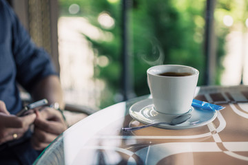 cup of coffee on a table in a cafe and men's hands with a phone in a blurry background