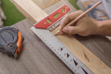 Hand of a carpenter measures the distance using a builder's square and marks it with a carpenter's...