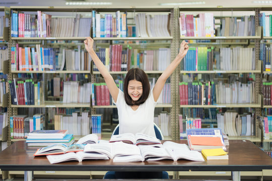 Young Asian cheerful woman student raise up hands celebrating ending of reading for exam in library at university.