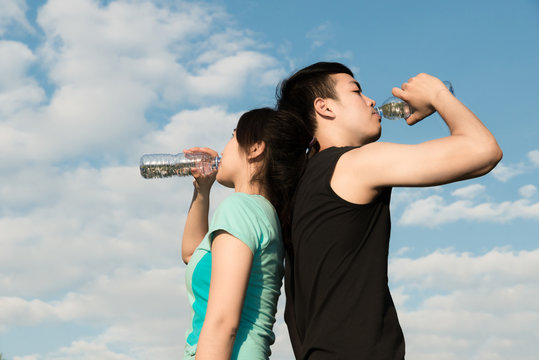Asian couple man and woman drinking water from bottle after fitness sport exercise.