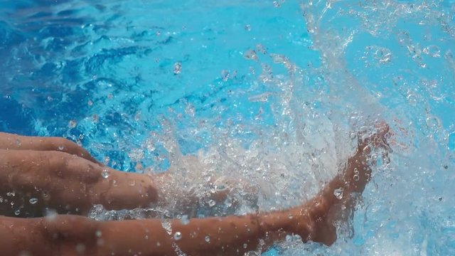Girls sitting on the edge of a pool dangling feets in the water.

