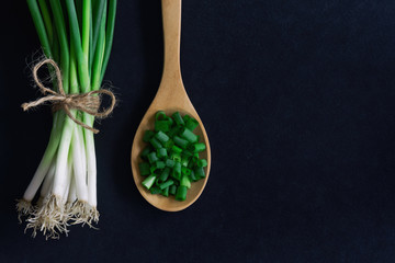 Fresh spring onion on black granite table. Close up on chopped scallions or spring onion in top view flat lay. Prepare spring onion for cooking. Food and vegetable concept for background or wallpaper.