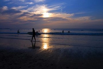 Fototapeta premium Silhouette of Night Surfer walking along the beach as sunset