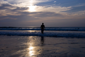 Fototapeta na wymiar Silhouette of Night Surfer walking along the beach as sunset