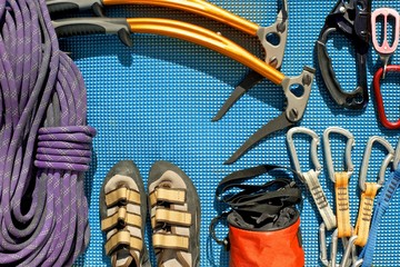 Climbing equipment laid out on a blue mat. Rope, ice tools, ascender, belay/rappel device with carabiner, quickdraws, chalk bag, climbing shoes. 