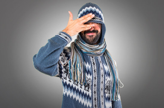 Man with winter clothes covering his eyes on grey background