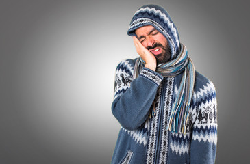 Man with winter clothes making sleep gesture on grey background