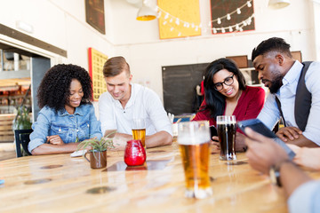 friends with smartphone, tablet pc and beer at bar